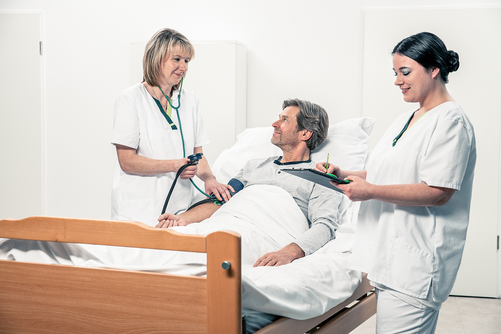 Patient liegt im Bett und wird von 2 Pflegekräften versorgt